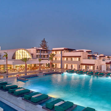 Paralos Kosta Alimia big pool with green sunbeds and a hotel building in the background at dusk