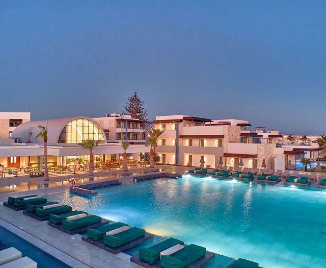 Paralos Kosta Alimia big pool with green sunbeds and a hotel building in the background at dusk