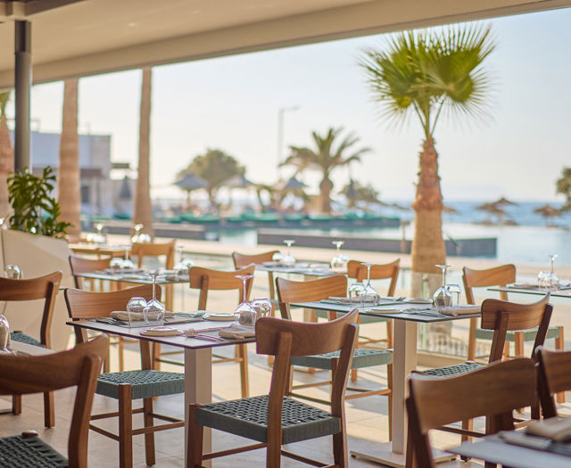 Paralos Kosta Alimia restaurant tables with wine glasses, plates and cutlery, chairs and the pool in the background